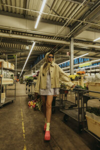 Model steht im beigen Trenchcoat und pinken crocs in einer Gärtnerei