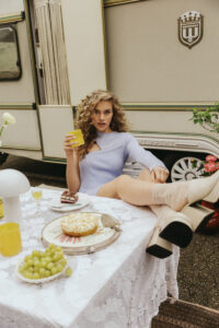 model im lila Kleid sitzt am Tisch mit den beinen auf dem Tisch und hält ein Glas Orangensaft in der Hand