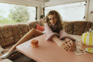 Model sitzt im Wohnwagen mit rosa Strickpullover