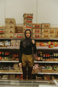 Model steht lässig in goldener kurzer hotpants und Kopftuch vor einem asiatischen Supermarkt